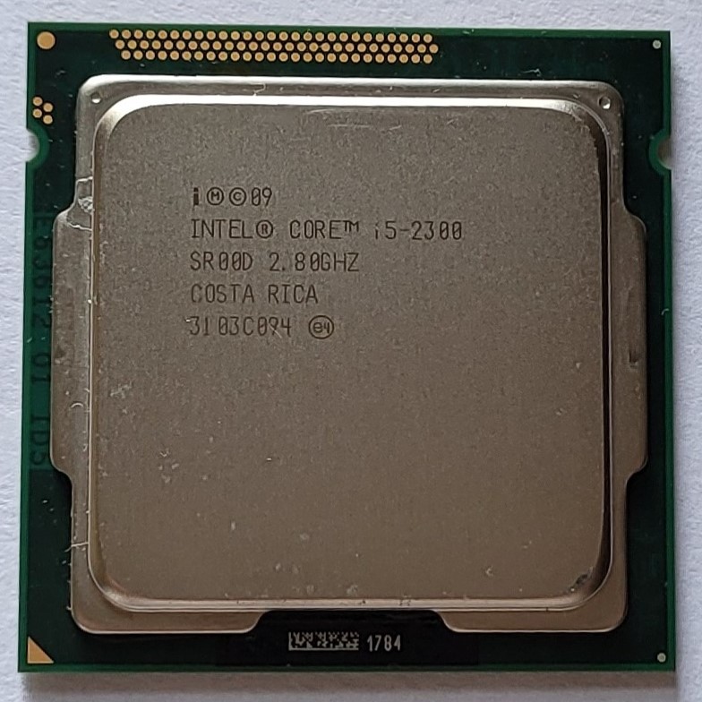 A top view of the square, nearly-flat silver-colored metal cpu chip: Intel Core i5-2300, 2.80GHZ, Made in Costa Rica.