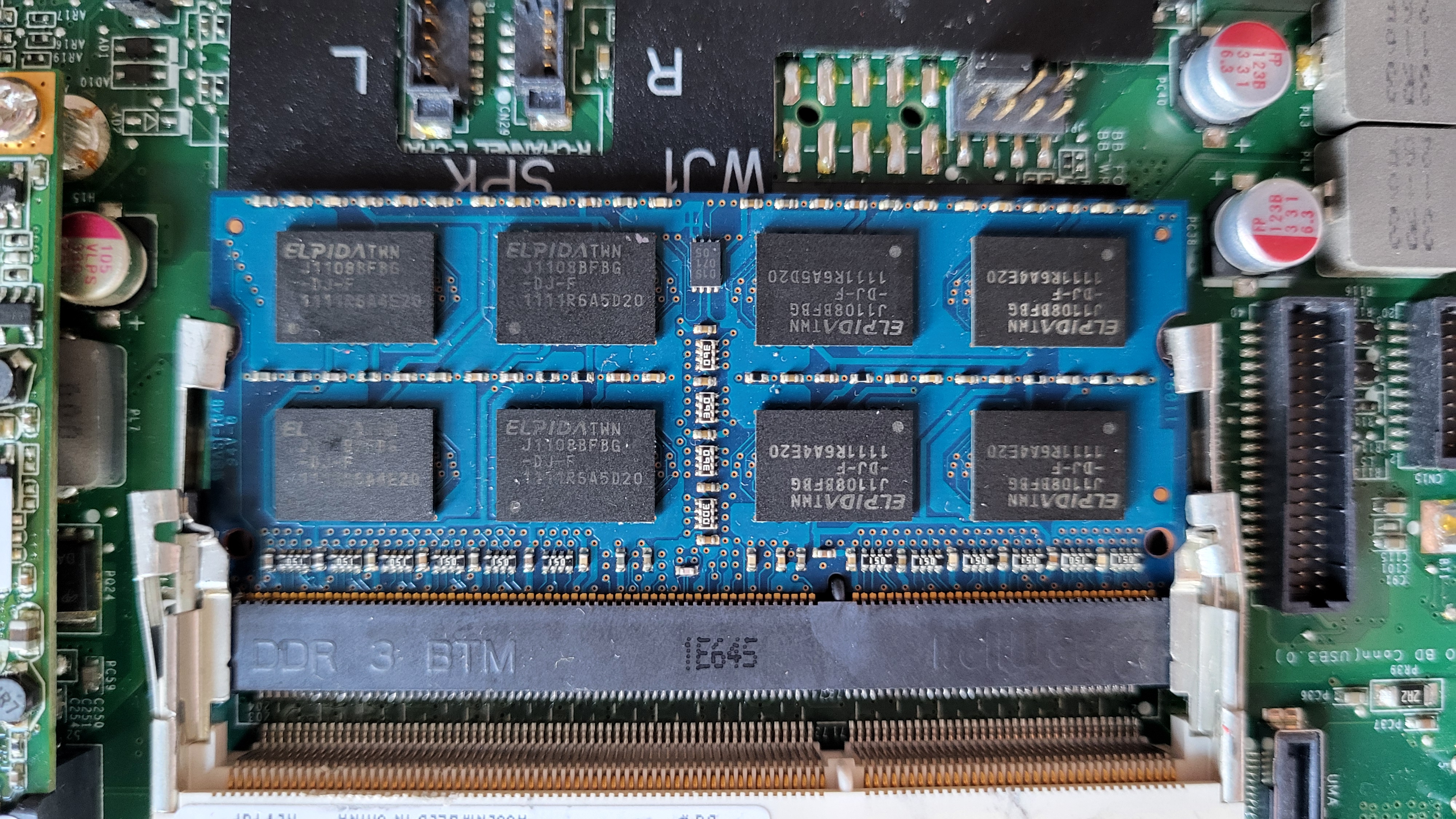 A closeup of the right-hand memory compartment on the computer's motherboard, showing a blue, rectangular, and flat memory chip (2GB) already inside.